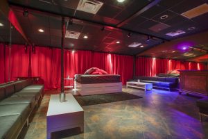 Our private videos are shot in Colette's VIP room with a bed in the center against a red curtain backdrop, viewing couches on two sides, and stained concrete floor.